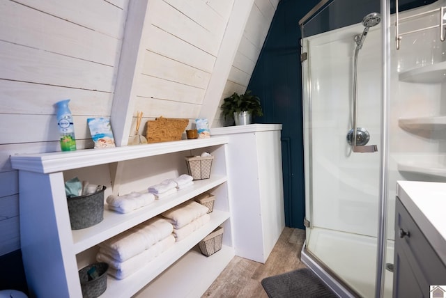 bathroom with hardwood / wood-style flooring, vaulted ceiling, a shower with shower door, and wood walls