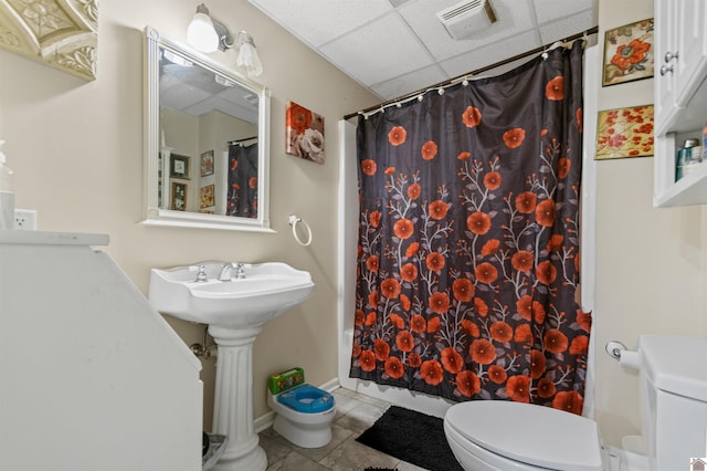 bathroom featuring tile patterned floors, toilet, and a drop ceiling