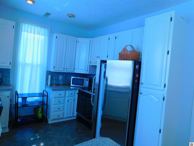 kitchen with appliances with stainless steel finishes, tasteful backsplash, dark tile patterned floors, and white cabinetry