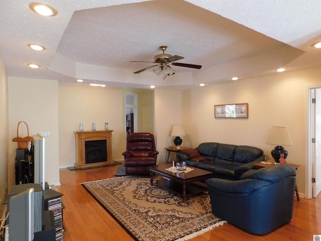 living room featuring ceiling fan, a textured ceiling, light wood-type flooring, and a tray ceiling