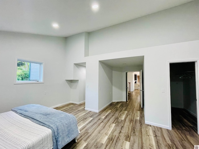 bedroom featuring high vaulted ceiling, a walk in closet, and hardwood / wood-style flooring