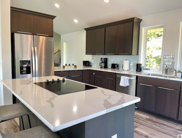 kitchen featuring appliances with stainless steel finishes, a kitchen bar, backsplash, light hardwood / wood-style flooring, and dark brown cabinetry