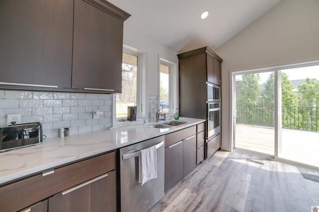 kitchen with decorative backsplash, stainless steel appliances, light hardwood / wood-style floors, light stone counters, and vaulted ceiling