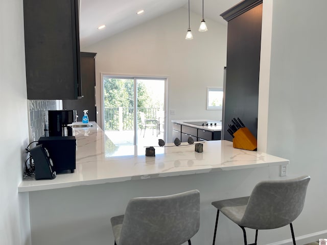 kitchen with kitchen peninsula, hanging light fixtures, light stone counters, and a breakfast bar area