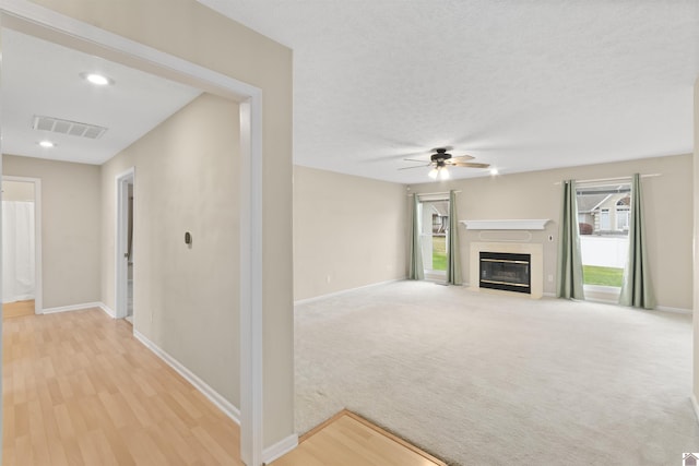 unfurnished living room featuring light carpet, a textured ceiling, and ceiling fan