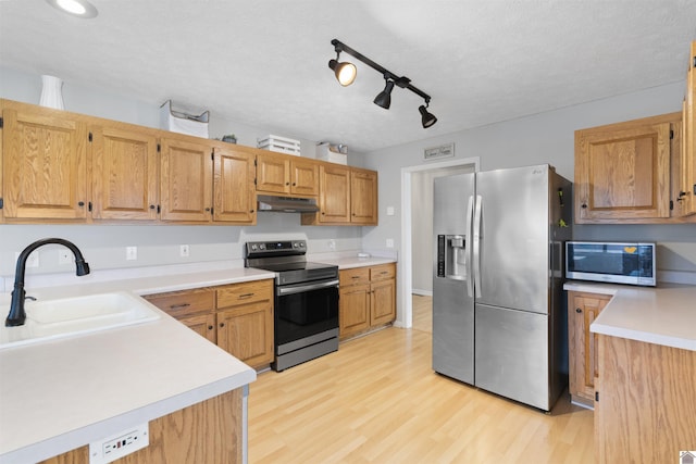 kitchen featuring appliances with stainless steel finishes, sink, a textured ceiling, and light wood-type flooring