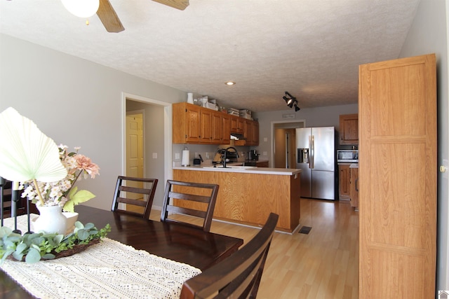 dining area featuring ceiling fan, sink, a textured ceiling, and light hardwood / wood-style floors