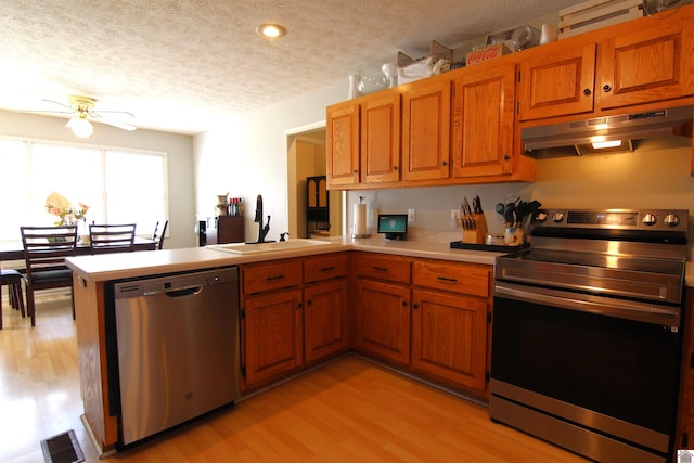 kitchen with appliances with stainless steel finishes, sink, kitchen peninsula, and light hardwood / wood-style floors