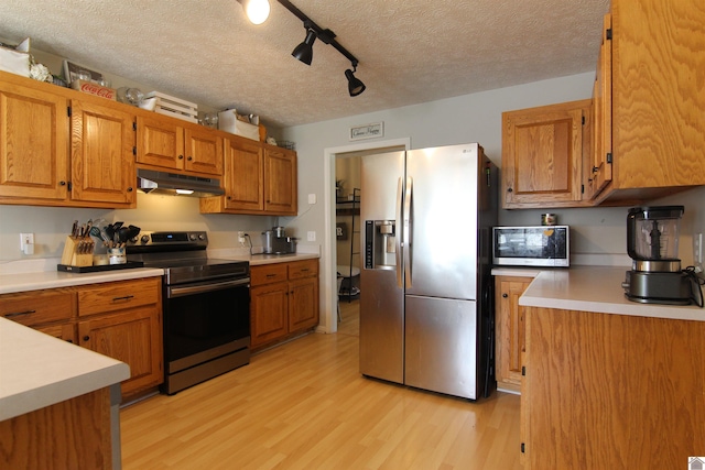 kitchen with appliances with stainless steel finishes, light hardwood / wood-style flooring, a textured ceiling, and track lighting