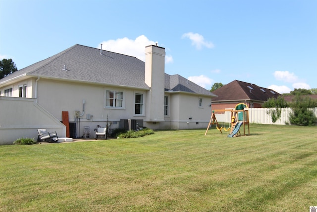 rear view of property with a playground, a yard, and central air condition unit