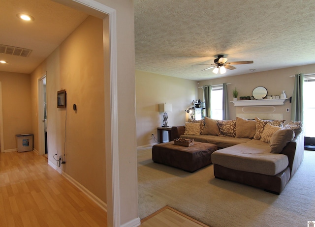 living room with light carpet, a textured ceiling, ceiling fan, and a healthy amount of sunlight