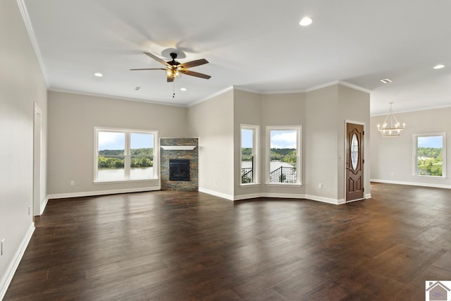 unfurnished living room featuring ceiling fan with notable chandelier, a wealth of natural light, a stone fireplace, and dark hardwood / wood-style flooring