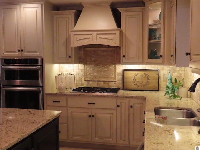 kitchen featuring stainless steel appliances, custom exhaust hood, backsplash, sink, and light stone counters