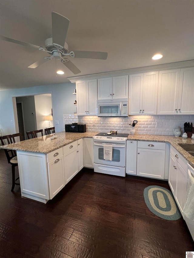 kitchen featuring dark hardwood / wood-style floors, ceiling fan, white cabinets, a kitchen breakfast bar, and white appliances