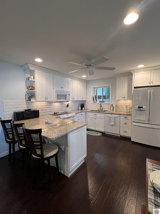 kitchen featuring white appliances, dark hardwood / wood-style floors, a kitchen breakfast bar, white cabinetry, and kitchen peninsula