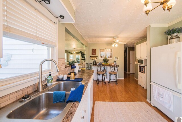 kitchen with white appliances, light wood finished floors, a sink, a textured ceiling, and white cabinetry