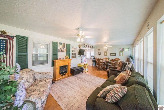 living room with ceiling fan, light wood-type flooring, and a textured ceiling