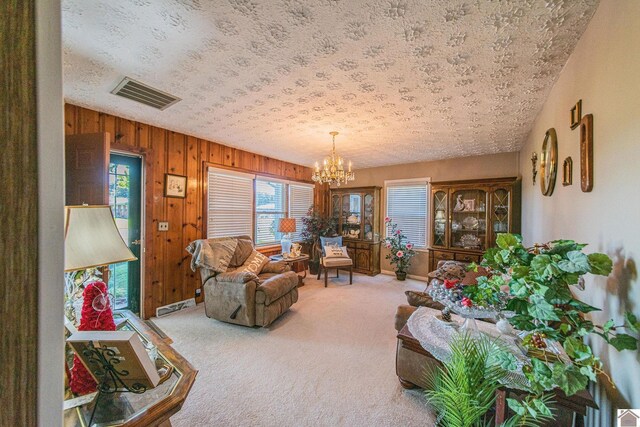 carpeted living room with a textured ceiling, wooden walls, and a chandelier