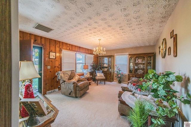 living room featuring visible vents, carpet floors, wood walls, a textured ceiling, and a notable chandelier