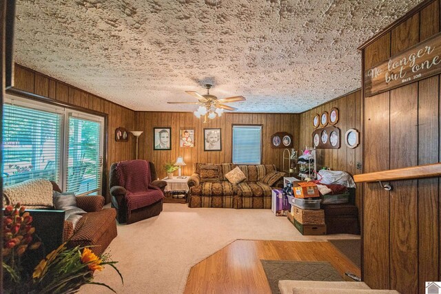 carpeted living room featuring ceiling fan, a textured ceiling, and wooden walls