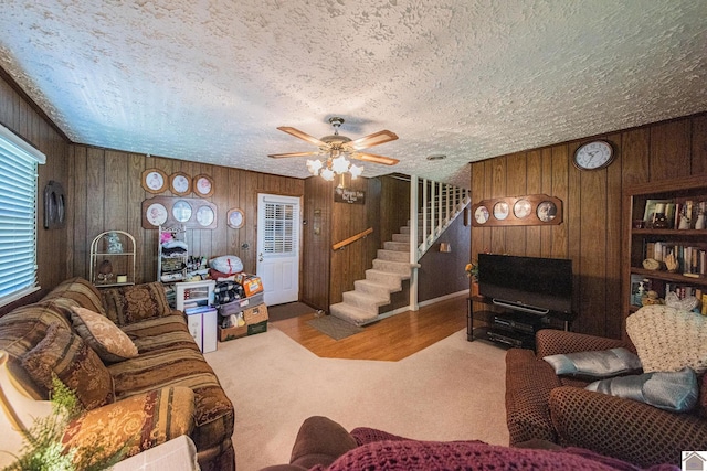 carpeted living room featuring ceiling fan, wood walls, and a textured ceiling