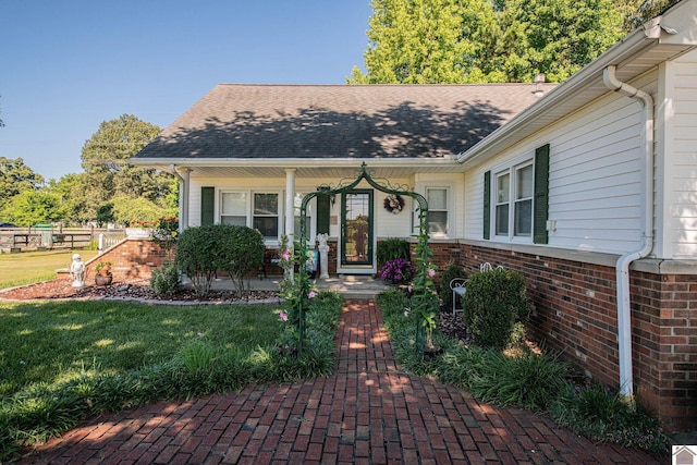 doorway to property with brick siding, a porch, a shingled roof, and a yard