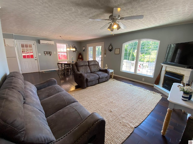 living room featuring dark wood-type flooring, ceiling fan with notable chandelier, an AC wall unit, and a textured ceiling