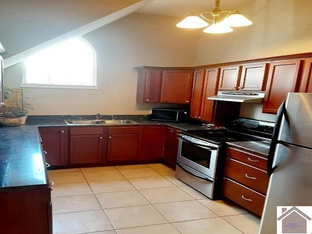 kitchen with sink, vaulted ceiling, appliances with stainless steel finishes, and light tile patterned flooring