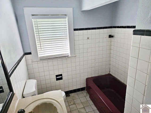 full bath with wainscoting, toilet, a bathing tub, tile patterned flooring, and tile walls