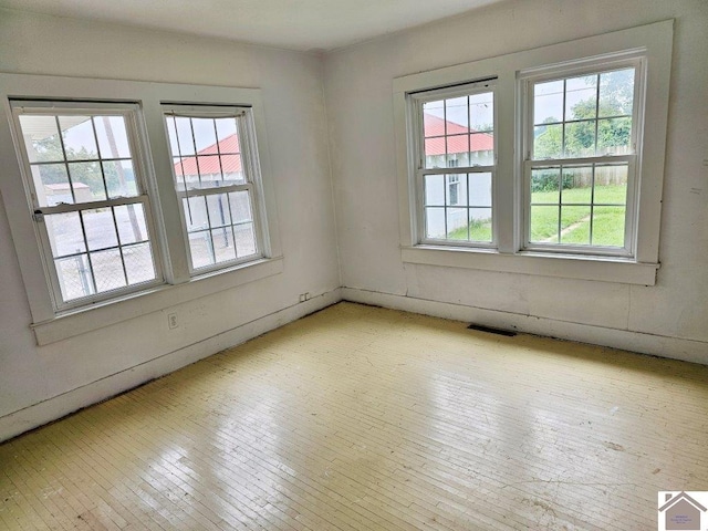 empty room featuring a wealth of natural light, visible vents, and light wood-style floors