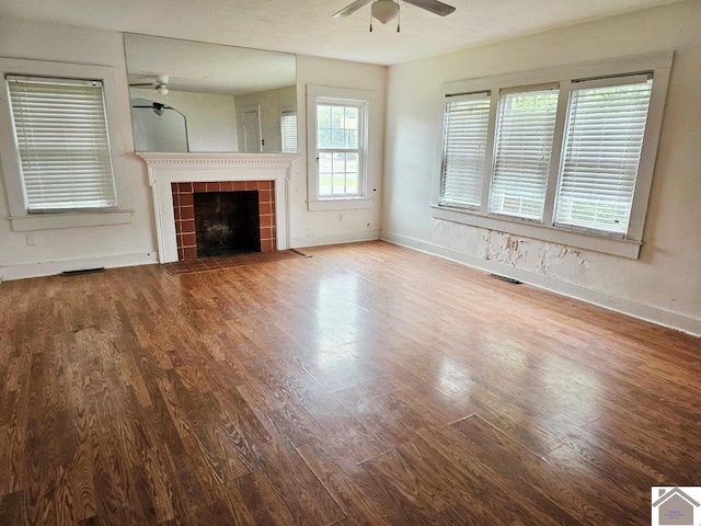 unfurnished living room with visible vents, ceiling fan, wood finished floors, a tile fireplace, and baseboards