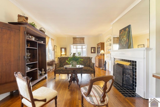 living area with dark wood-type flooring, a tile fireplace, and ornamental molding