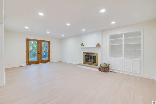 unfurnished living room with built in shelves, french doors, a fireplace, and light hardwood / wood-style flooring