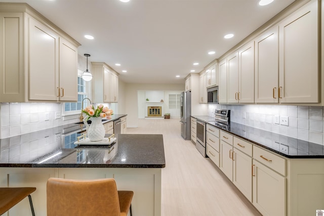 kitchen with light wood-type flooring, tasteful backsplash, stainless steel appliances, hanging light fixtures, and a breakfast bar area