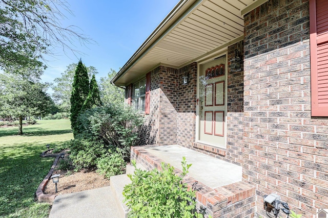 entrance to property with brick siding, a yard, and a patio