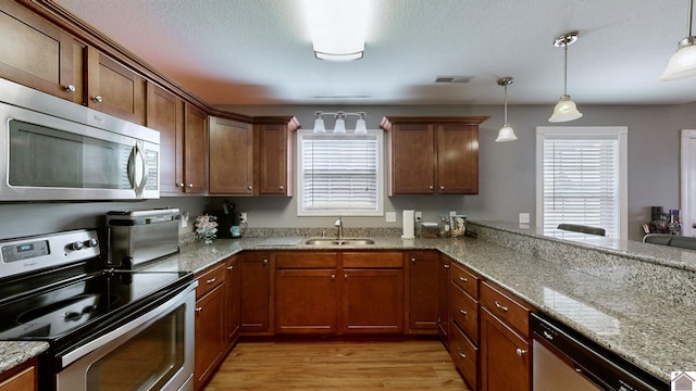 kitchen featuring sink, light wood-type flooring, decorative light fixtures, and appliances with stainless steel finishes