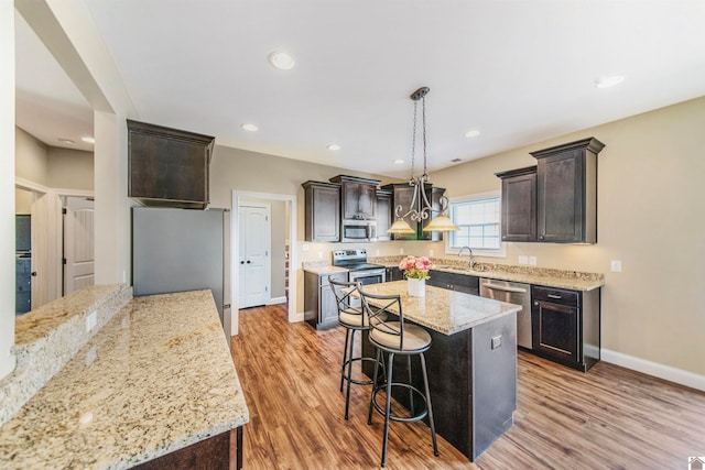 kitchen featuring appliances with stainless steel finishes, dark brown cabinetry, light wood-type flooring, a kitchen island, and hanging light fixtures