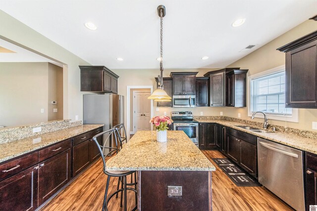 kitchen featuring decorative light fixtures, light hardwood / wood-style flooring, light stone countertops, a kitchen island, and stainless steel appliances