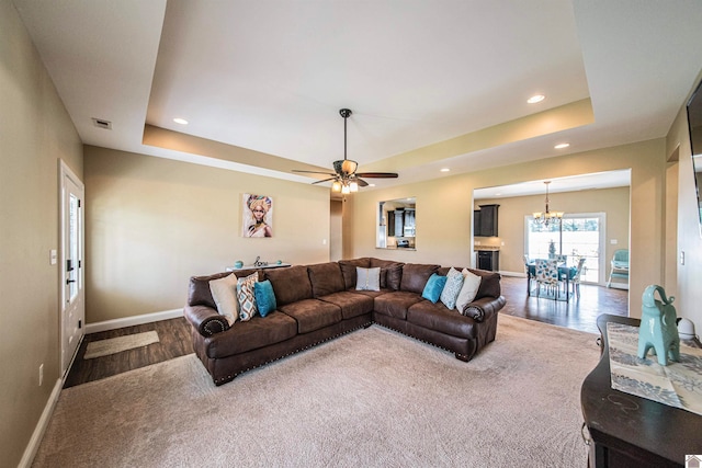 living room featuring ceiling fan with notable chandelier, dark hardwood / wood-style flooring, and a tray ceiling