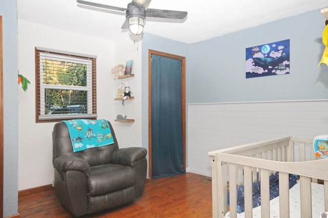 bedroom with ceiling fan, dark hardwood / wood-style floors, and a nursery area