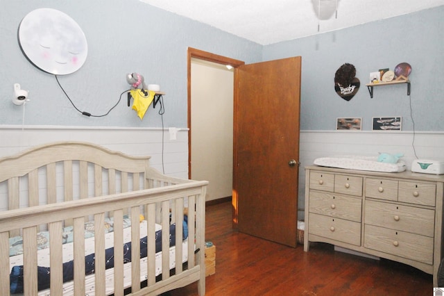 bedroom with a nursery area and dark hardwood / wood-style floors