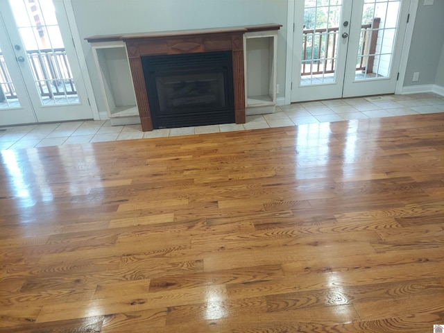 unfurnished living room with light wood-type flooring, a tiled fireplace, and french doors