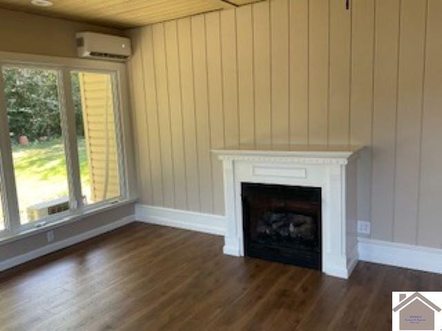 unfurnished living room featuring dark wood-type flooring, wood walls, an AC wall unit, and a healthy amount of sunlight