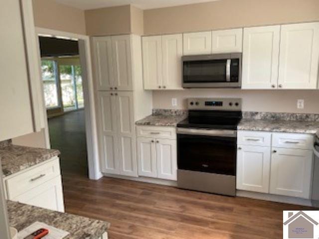 kitchen with appliances with stainless steel finishes, white cabinetry, light stone countertops, and dark hardwood / wood-style floors