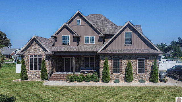 craftsman-style house featuring stone siding, a front lawn, roof with shingles, and a porch