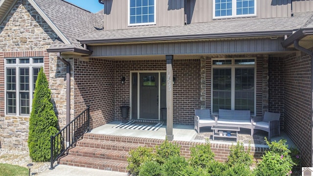 view of exterior entry featuring board and batten siding, stone siding, brick siding, and roof with shingles