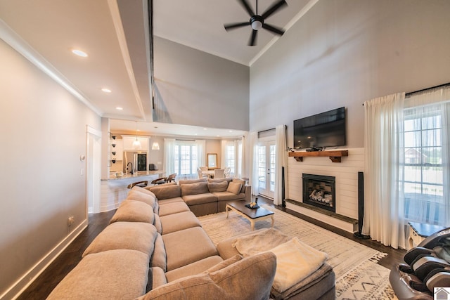 living room with a high ceiling, hardwood / wood-style floors, ceiling fan, and a large fireplace