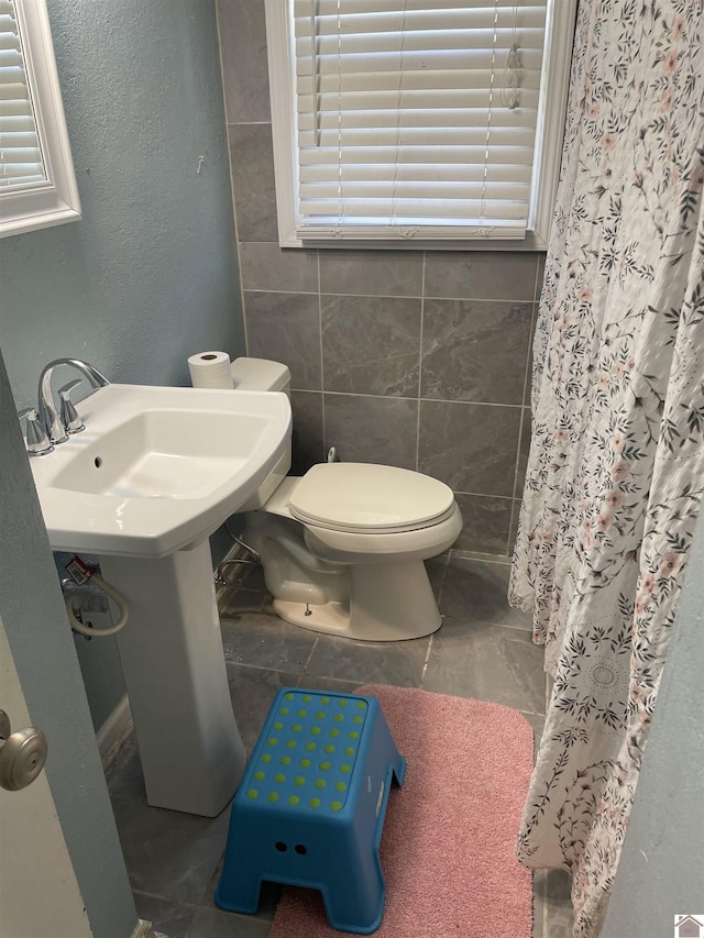 bathroom with a shower with curtain, toilet, and tile walls