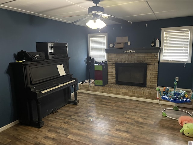 living room with a brick fireplace, a drop ceiling, baseboards, and wood finished floors