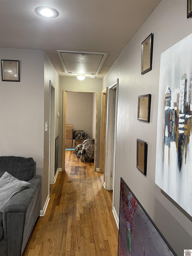 corridor featuring attic access, baseboards, and wood finished floors